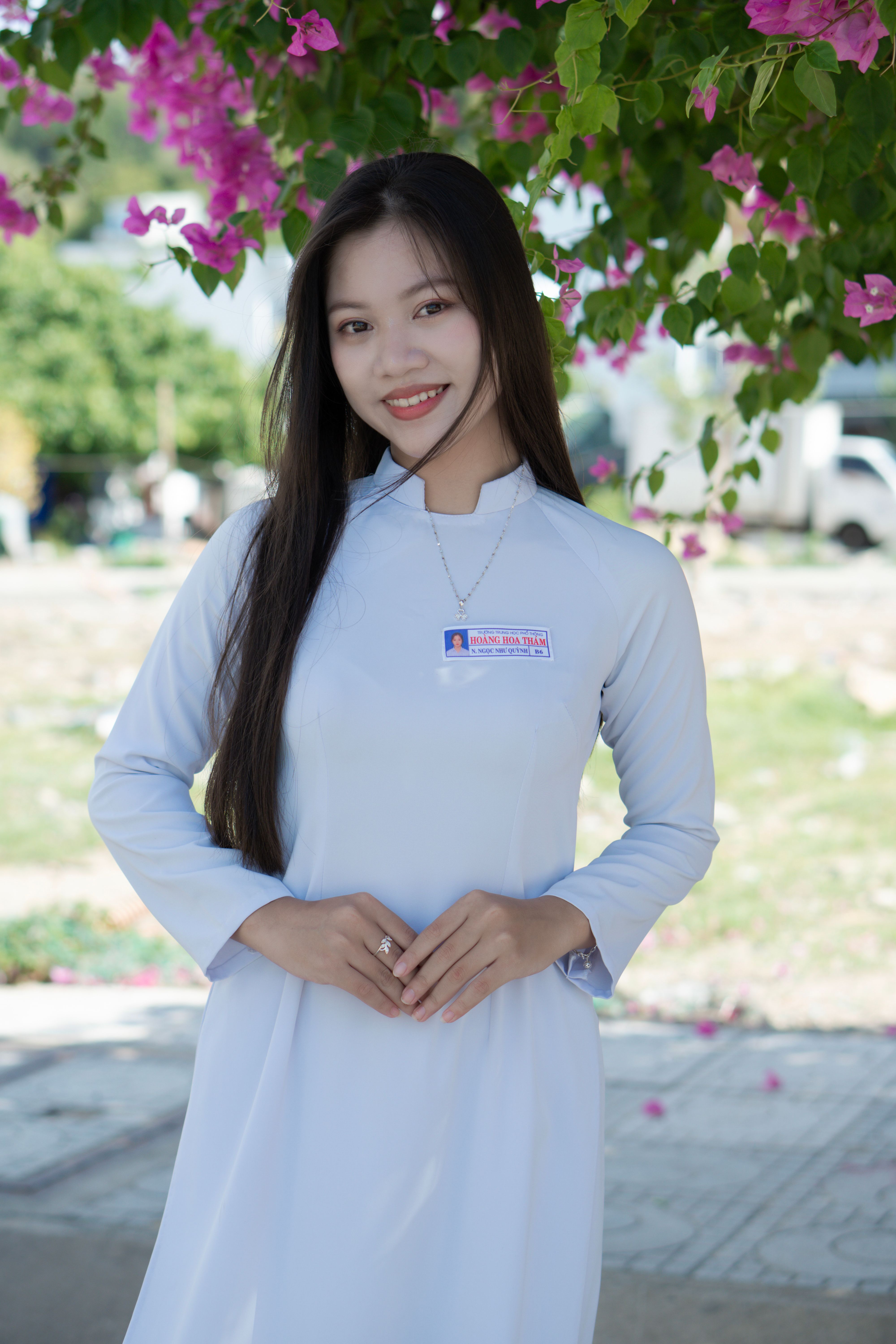 A beautiful woman in traditional attire smiles gracefully, surrounded by nature's bloom.