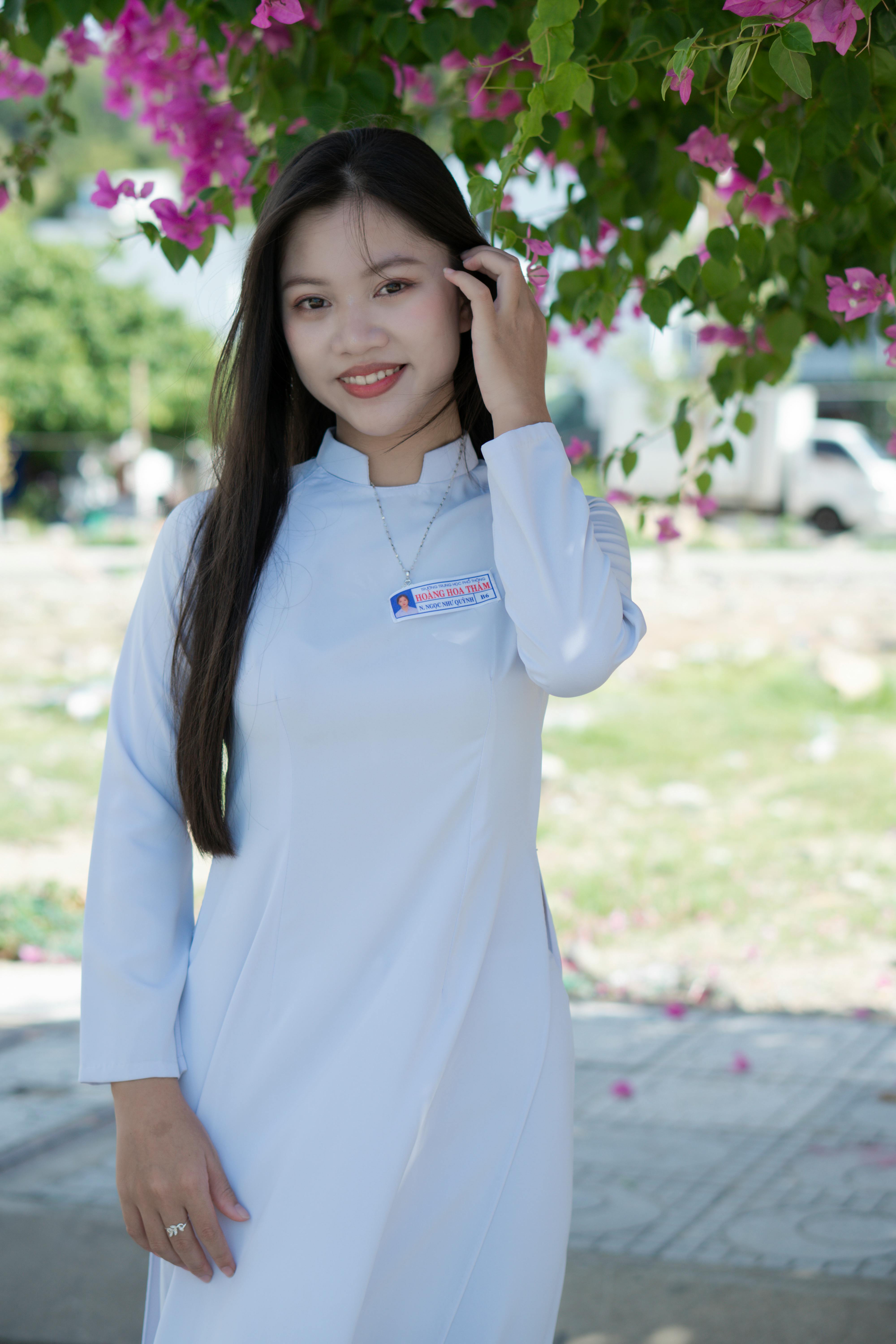 Portrait of a smiling woman in traditional white dress standing outdoors with flowers.