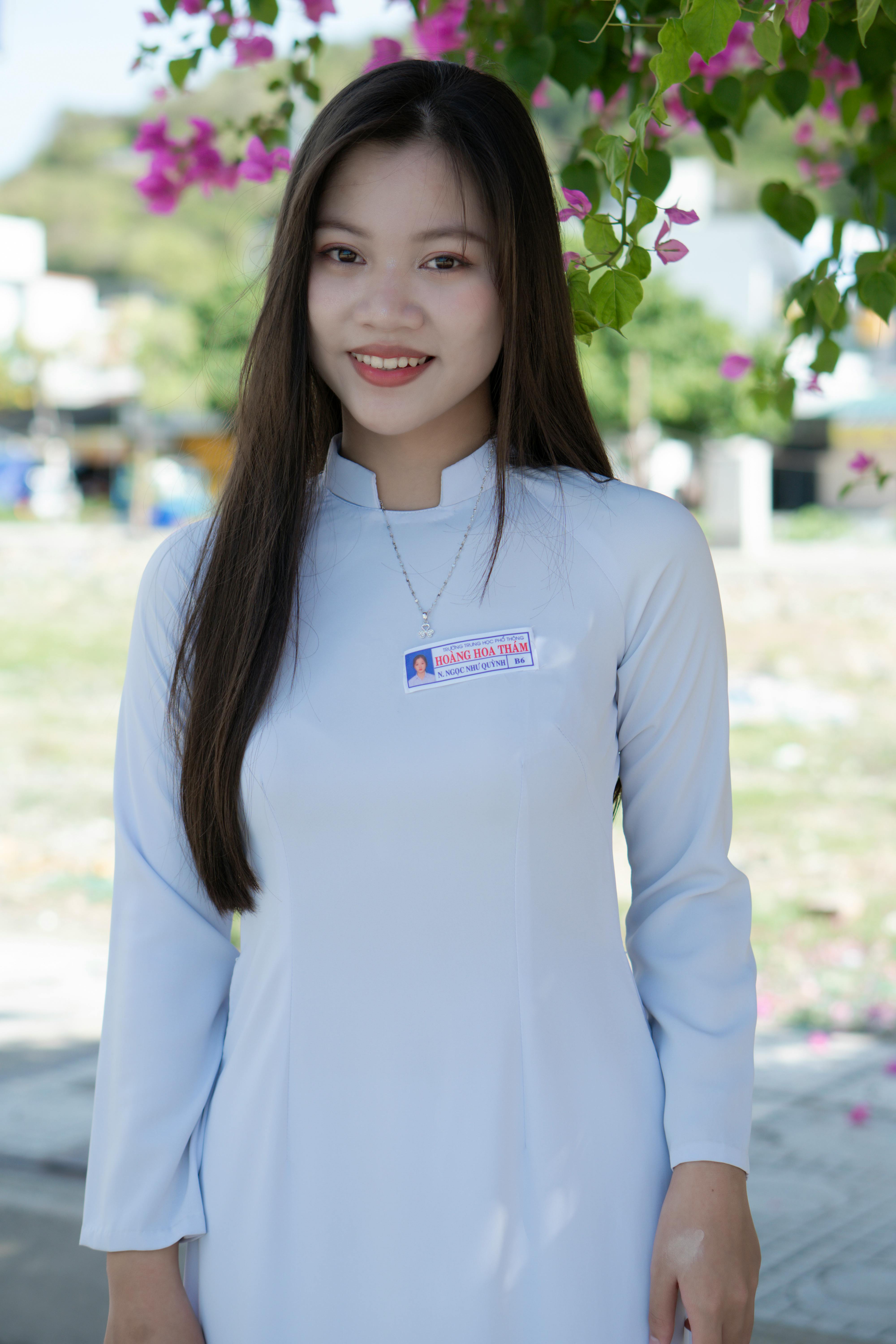 Portrait of a smiling woman in a traditional white dress standing outdoors under bright floral decorations.