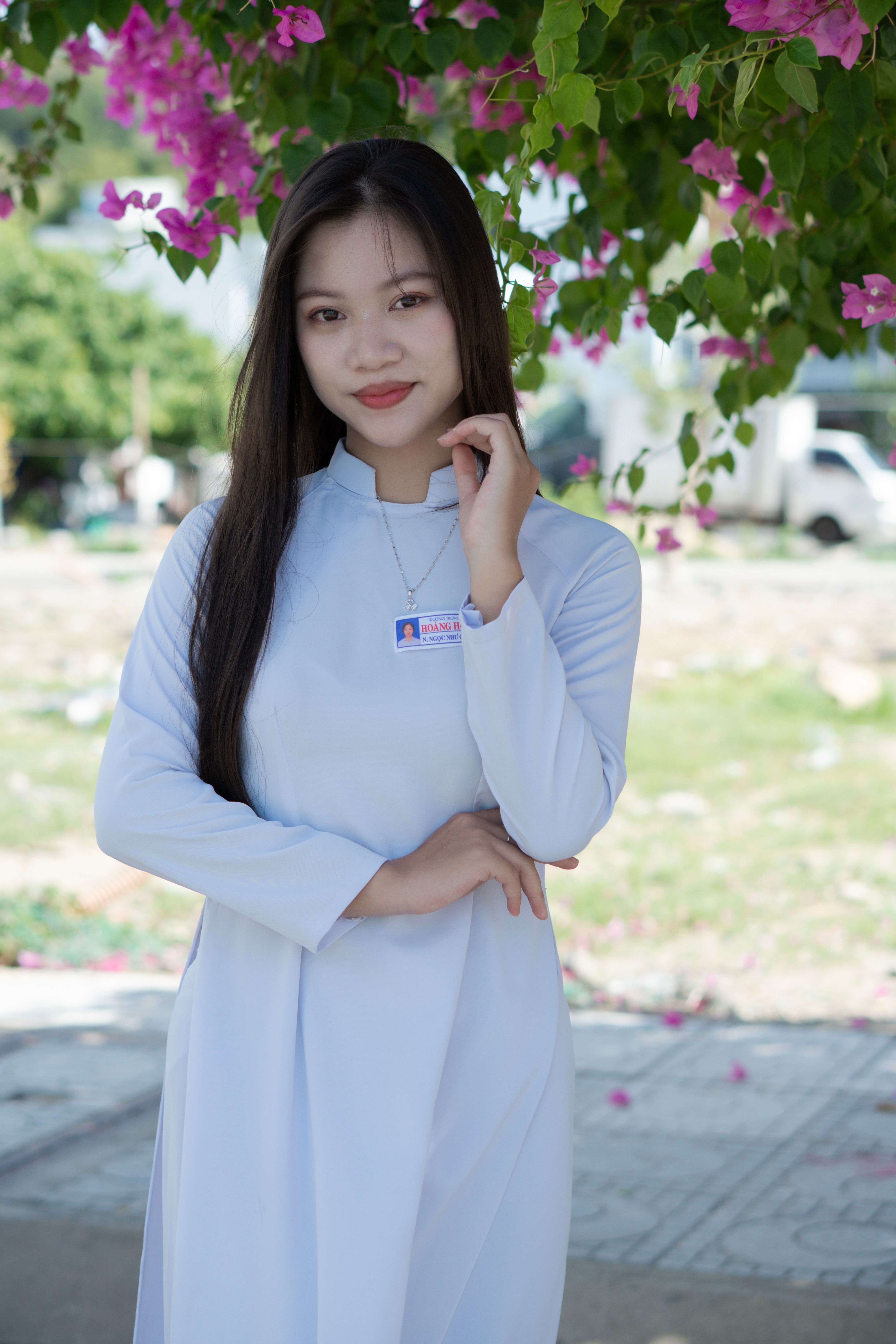 Portrait of a woman in white traditional dress, posing outdoors under flowering branches.