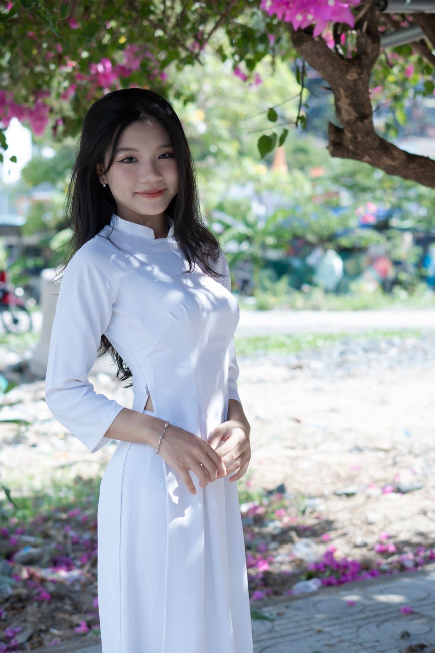 Asian woman in traditional white ao dai dress standing outdoors, exuding elegance and grace.