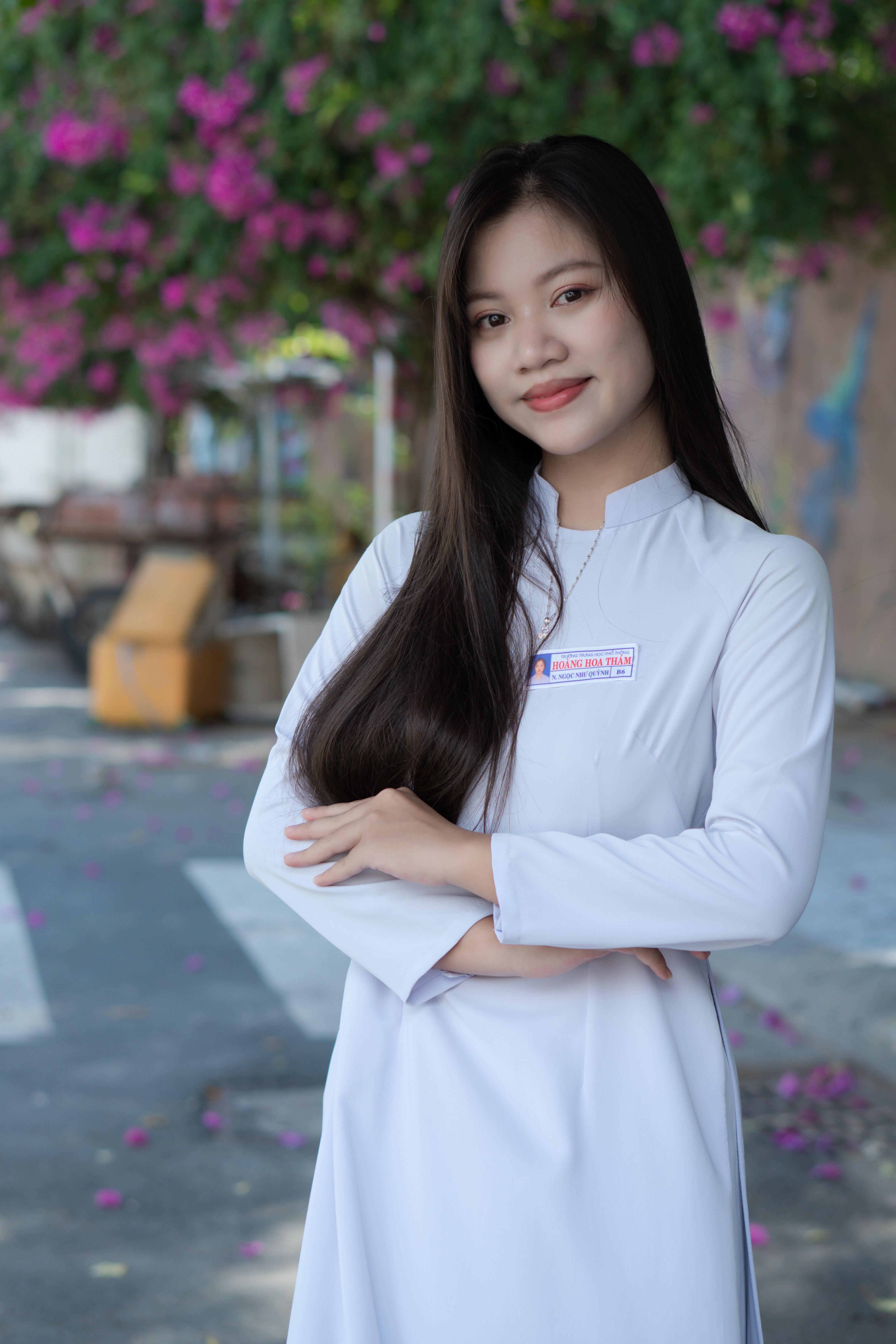 Portrait of an elegant woman in a white dress standing on blooming street.