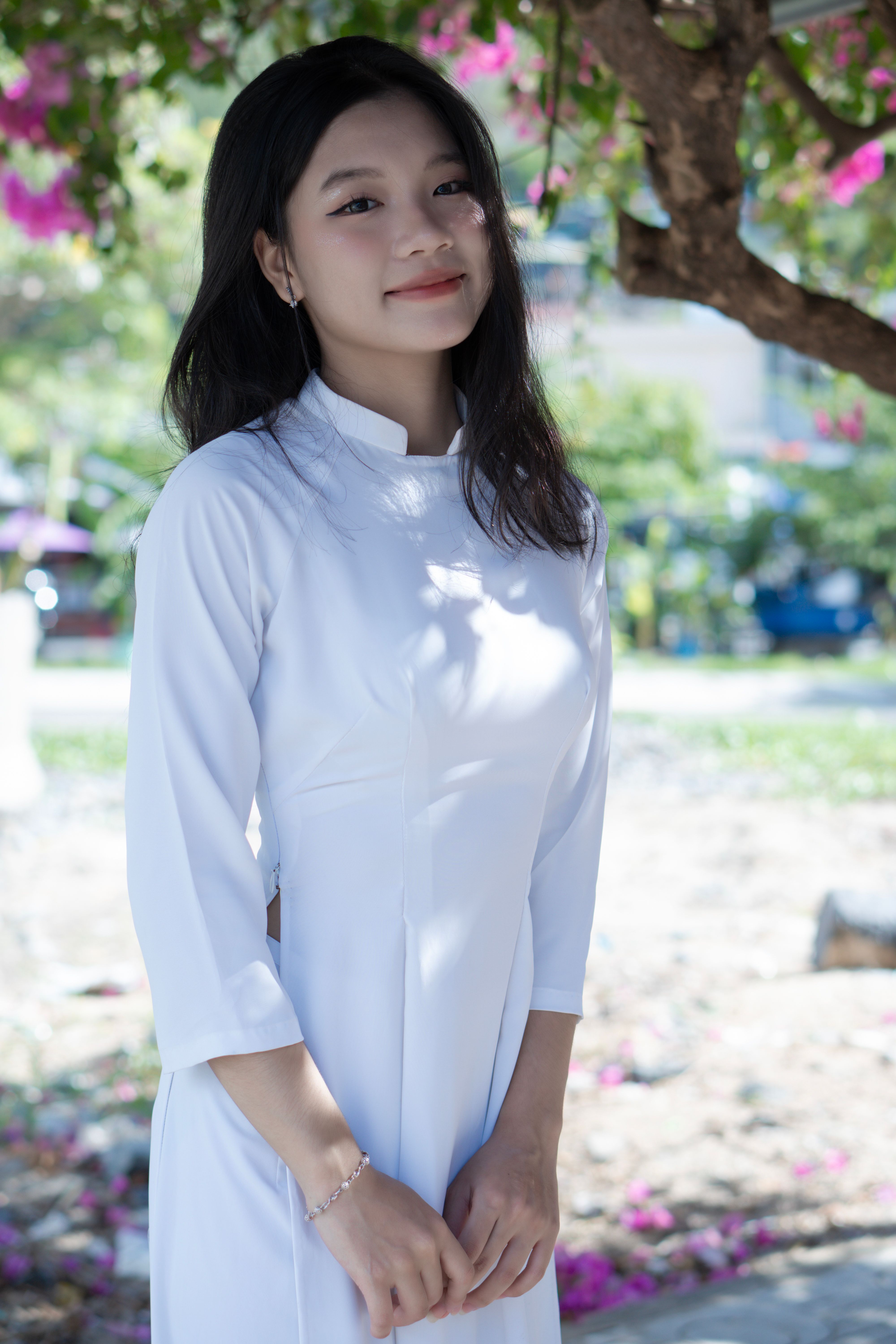 Portrait of a smiling woman in a white Ao Dai standing outdoors, exuding elegance.