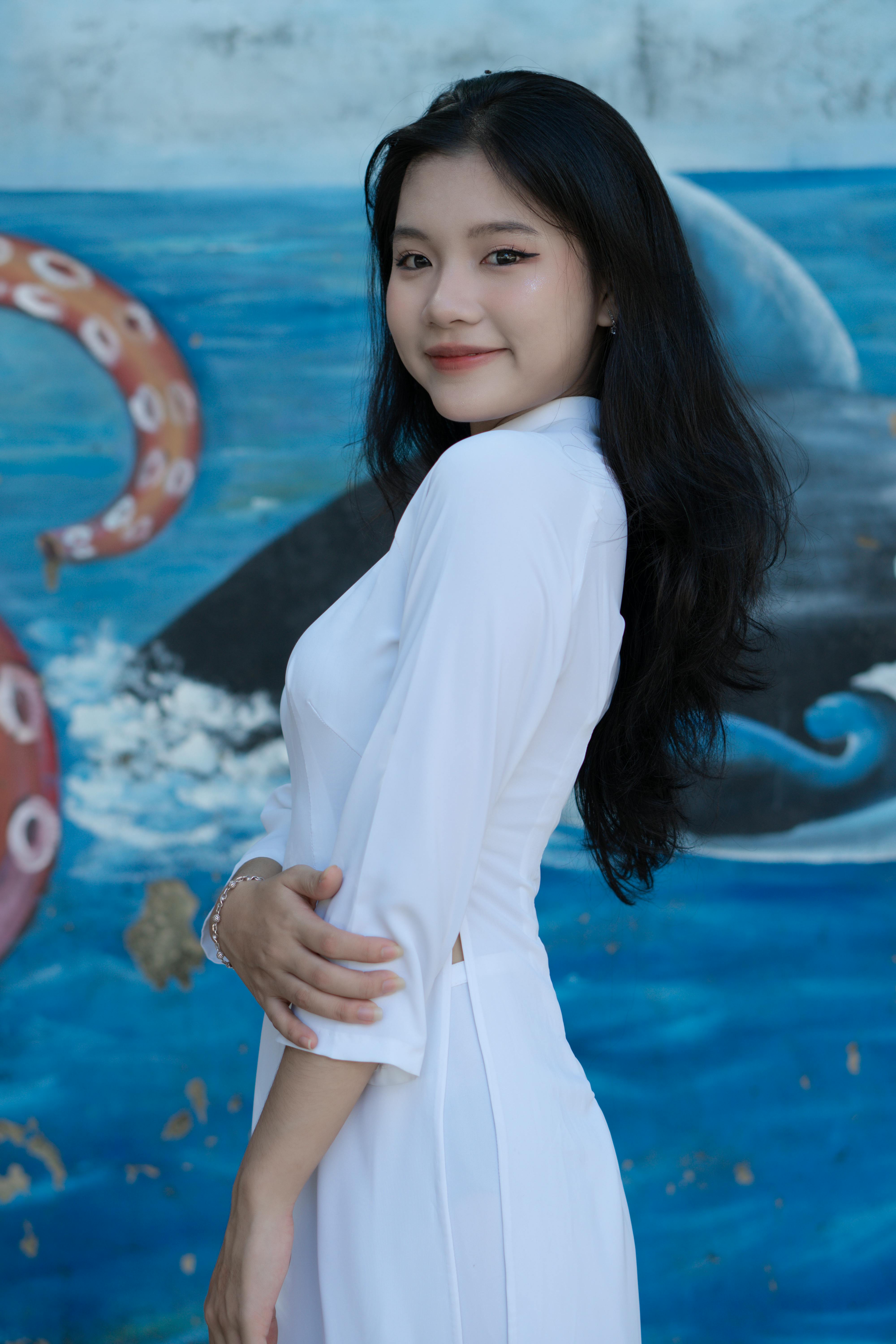 Asian woman elegantly posing in traditional white ao dai, with colorful mural backdrop.