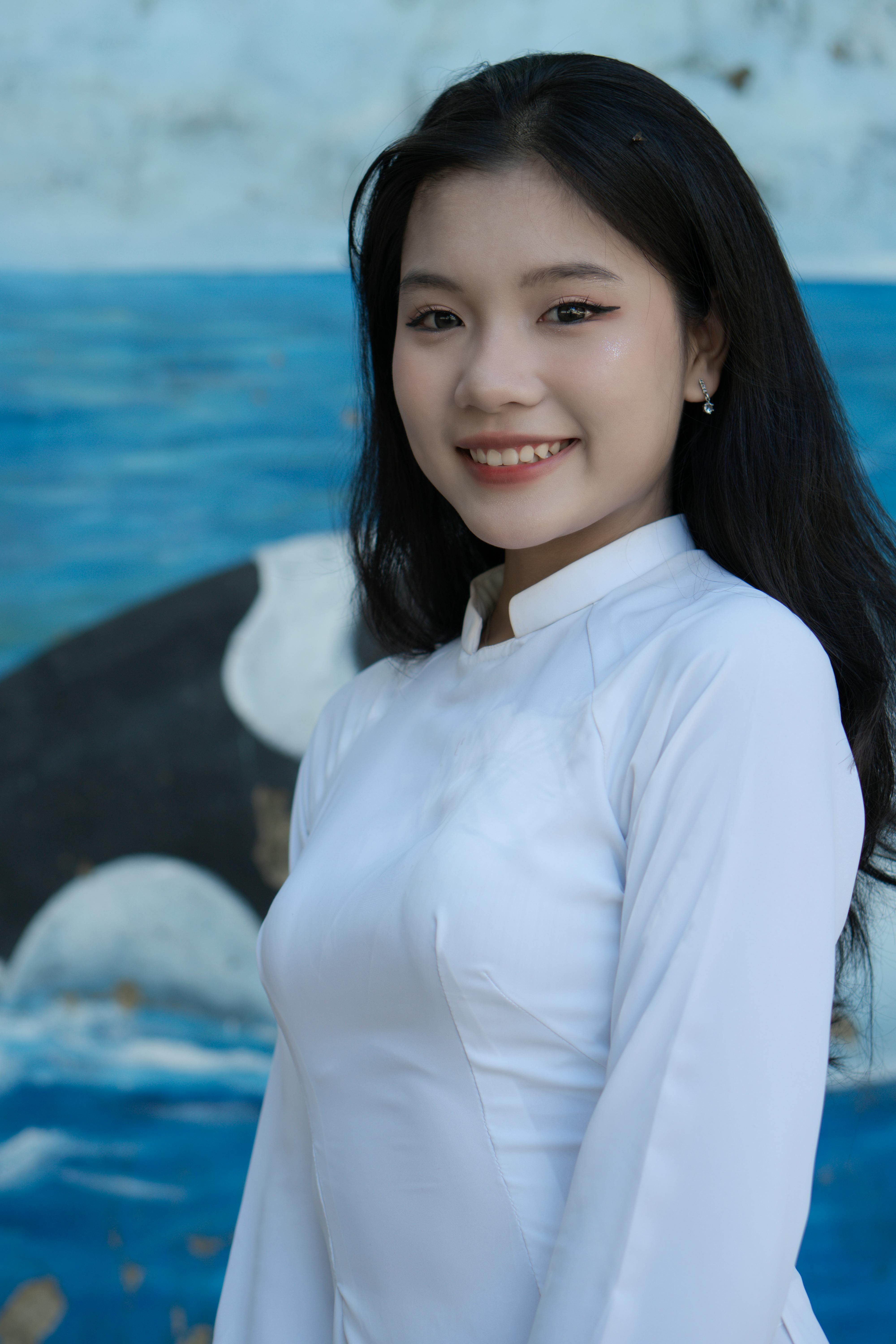 Portrait of a smiling woman in traditional white dress against artistic backdrop.