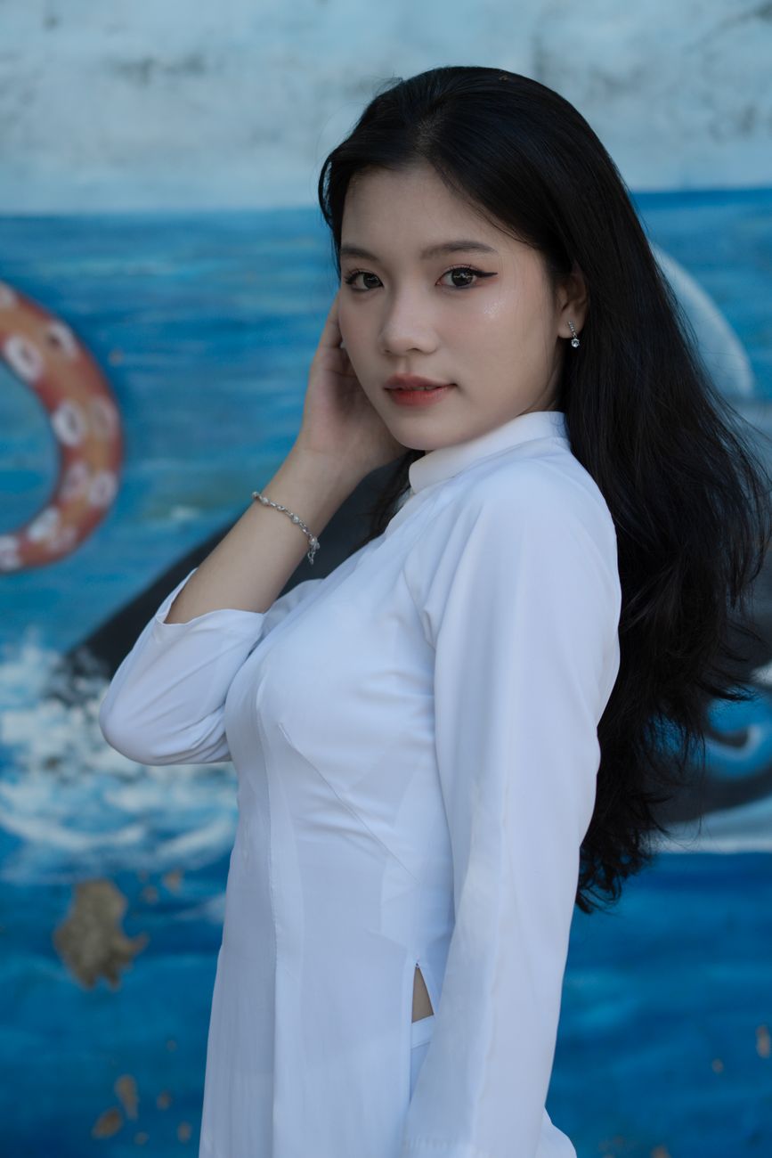 Elegant young woman posing in white Ao Dai against a colorful backdrop.