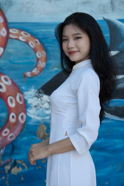 Free A woman in traditional white dress poses gracefully in front of an ocean-themed mural. Stock Photo