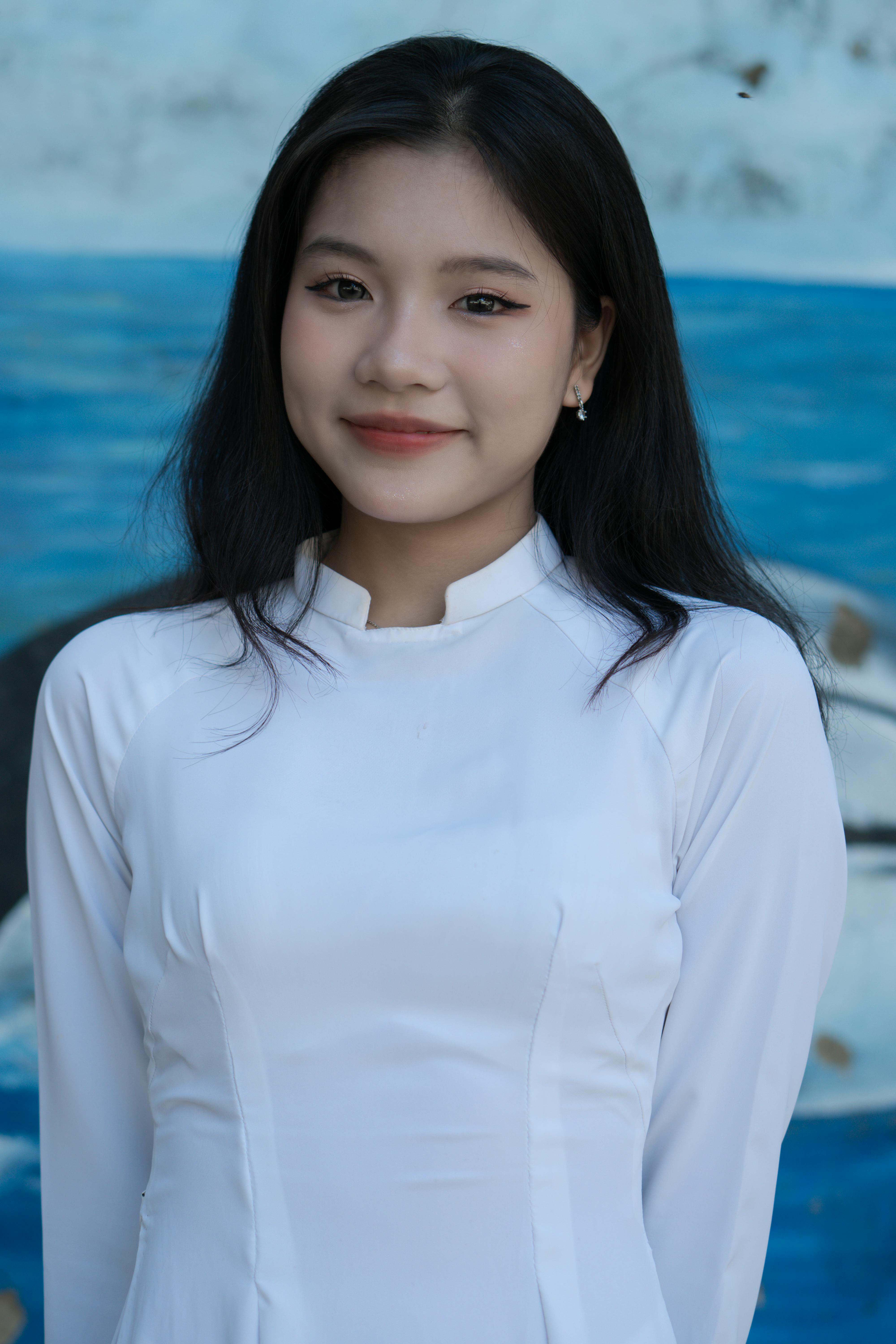 Portrait of a smiling young woman in a white dress with a blue artistic background.