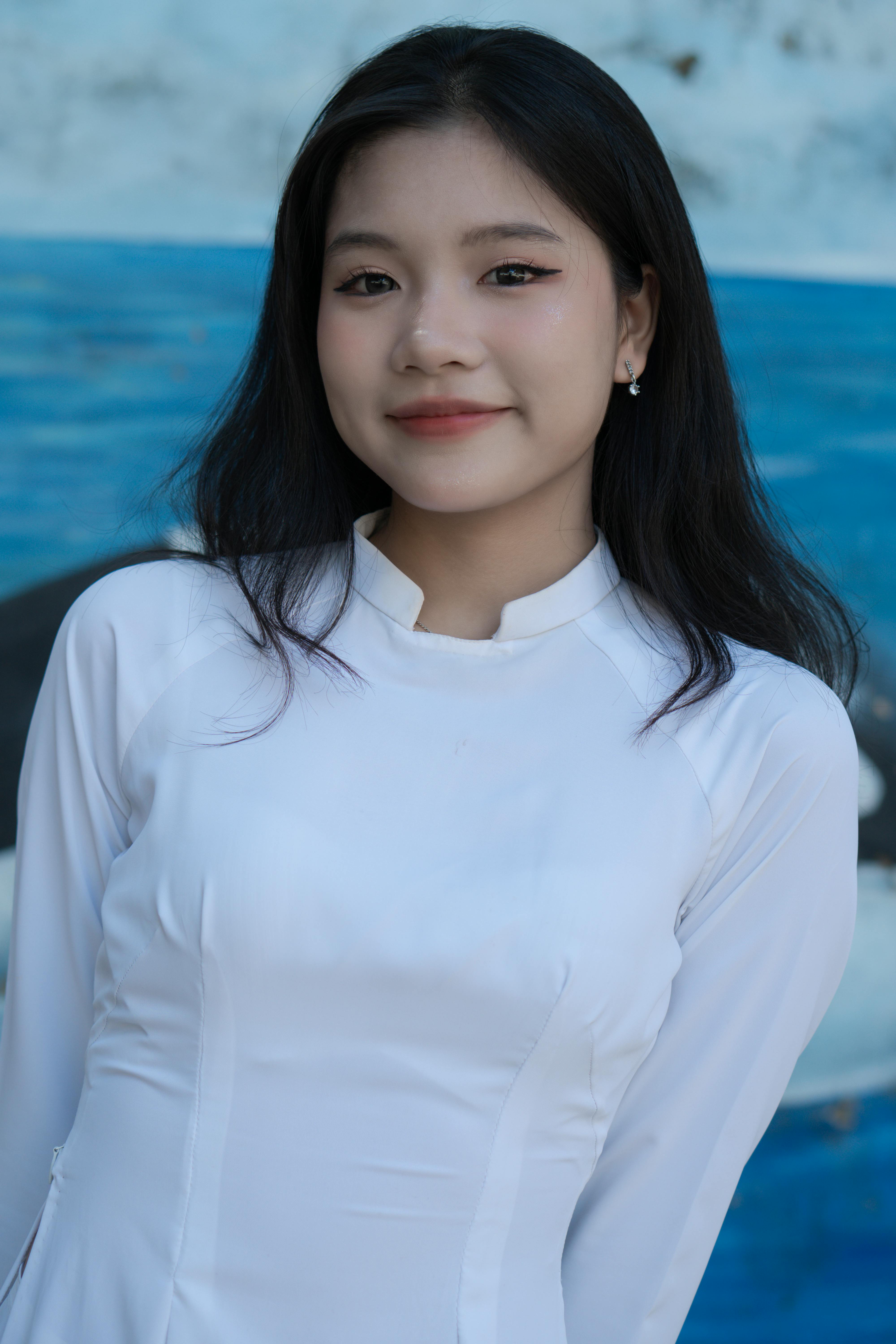 Portrait of a smiling young woman in white traditional attire, posing outdoors.