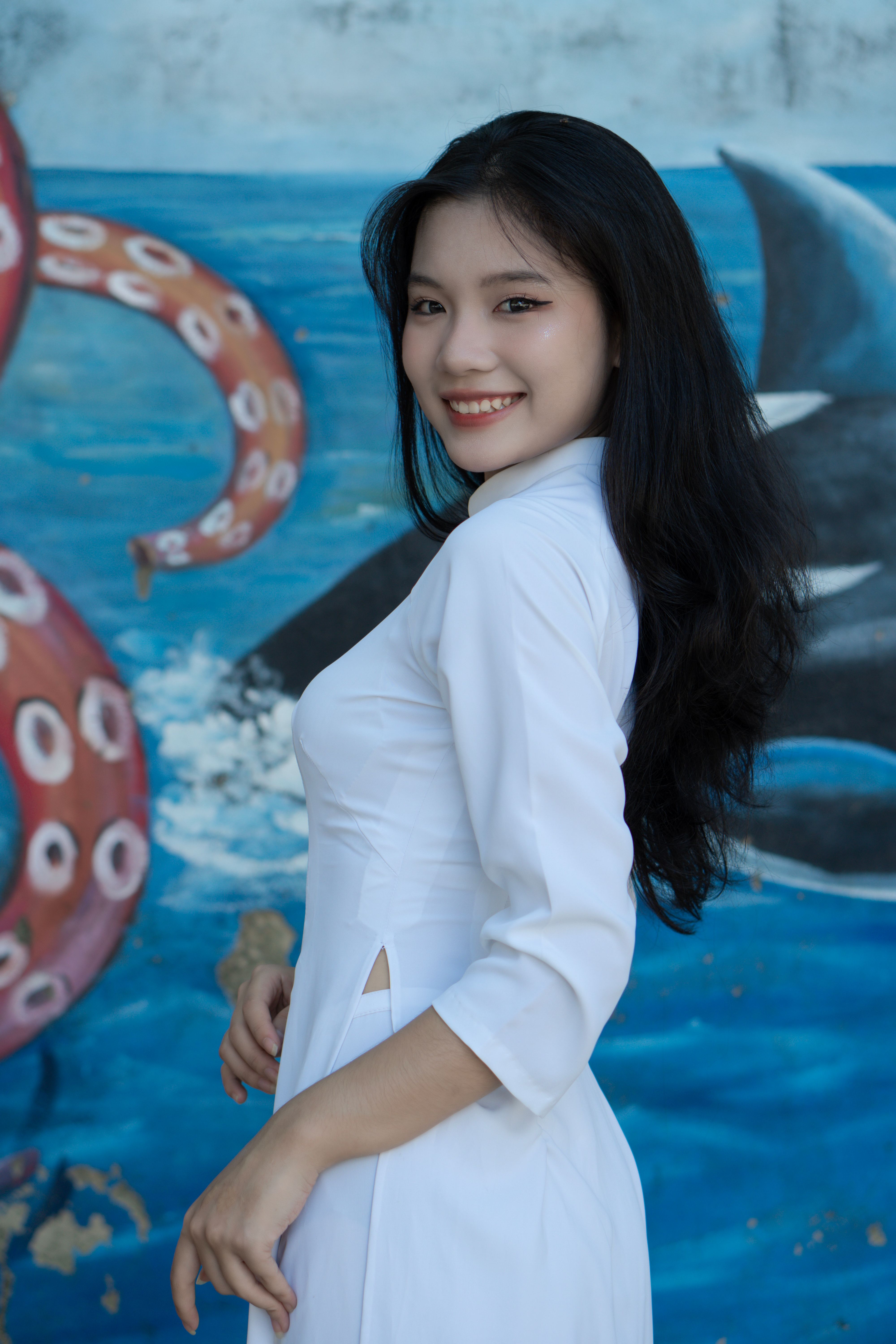 Stylish young woman poses in traditional Vietnamese ao dai against a lively mural background.