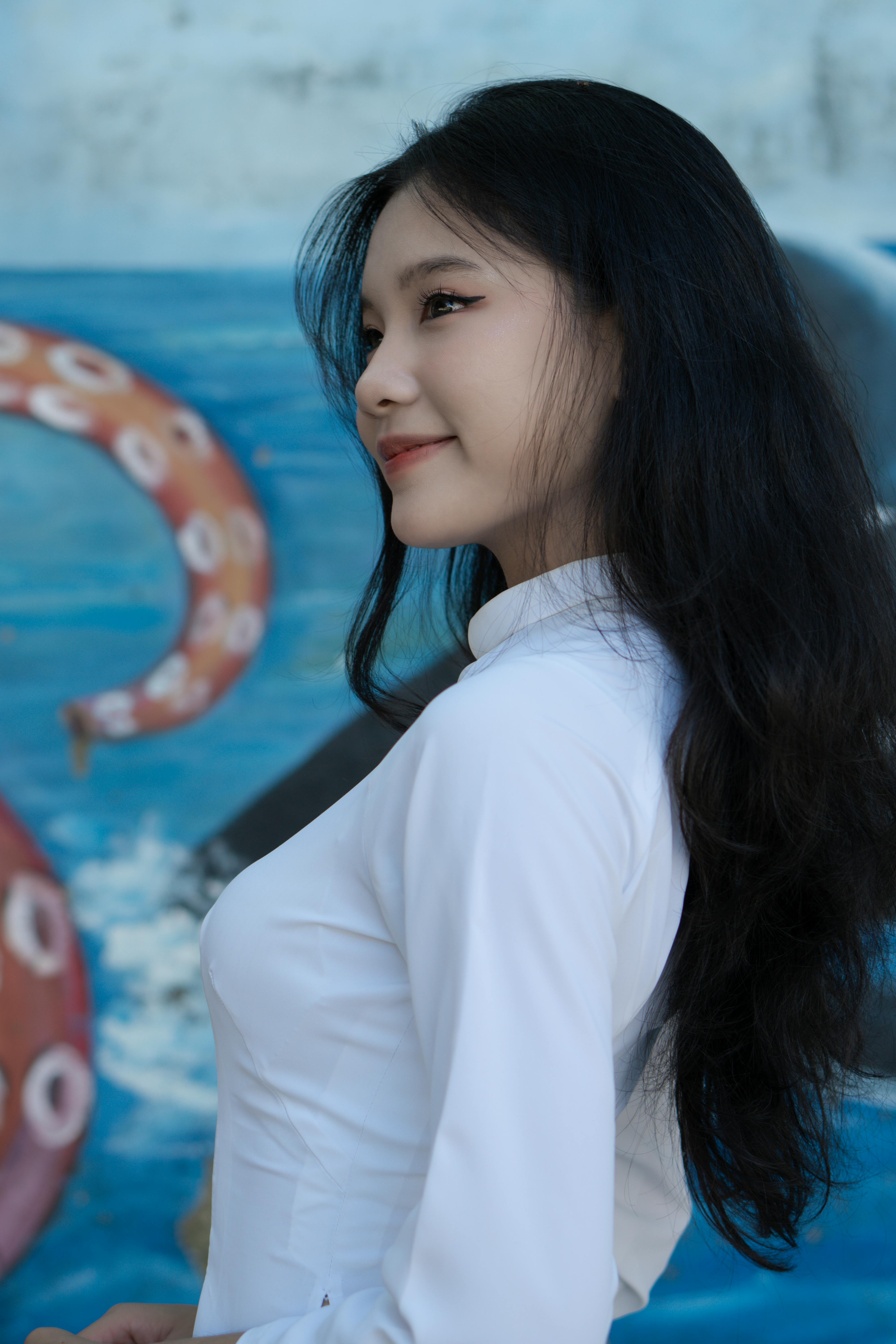 Captivating portrait of a smiling woman with long hair in a white dress, shot outdoors with colorful background.