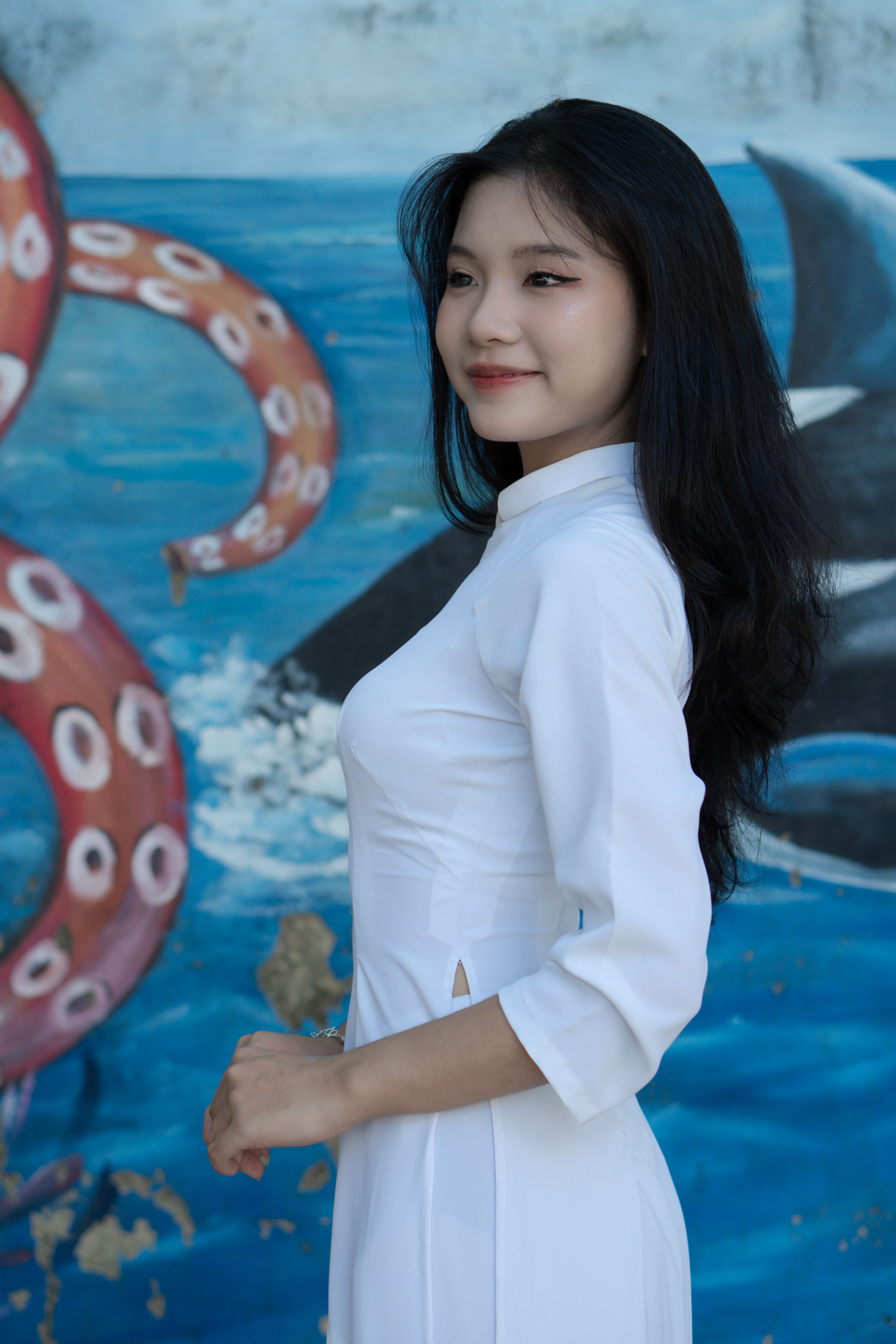 Young Vietnamese woman in ao dai with a vibrant mural background.