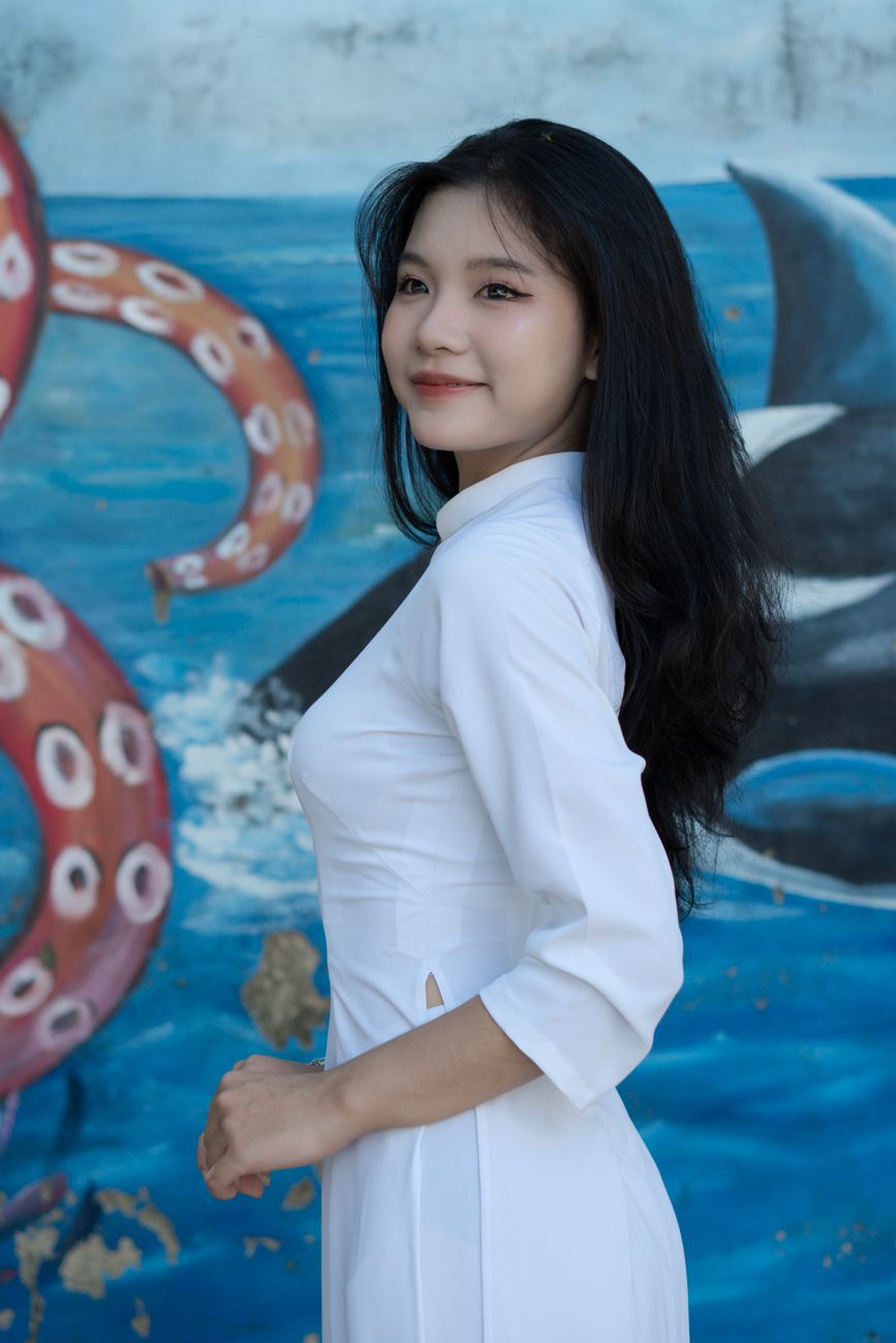 Beautiful young Vietnamese woman in a white ao dai posing outdoors.