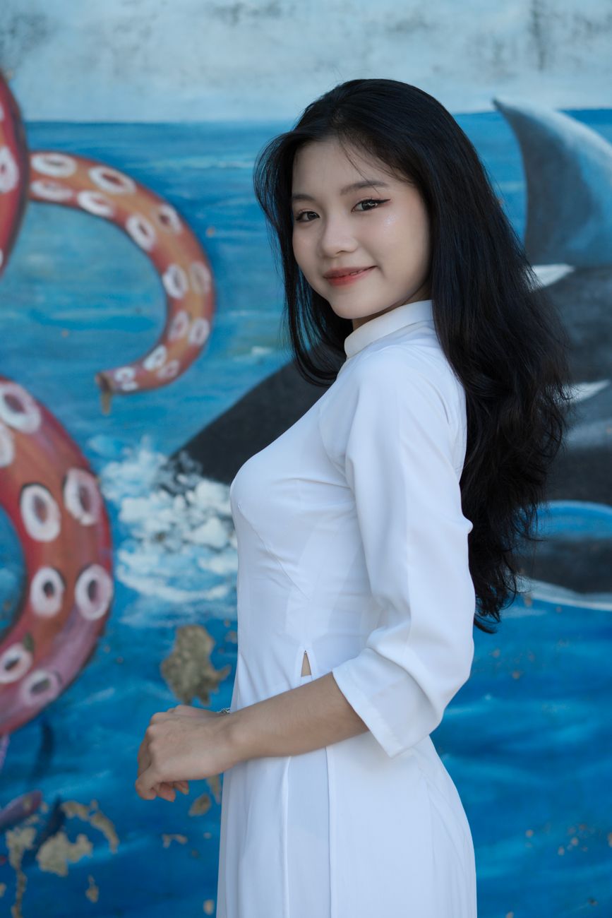 Smiling woman in a white ao dai posing against a vibrant ocean background.