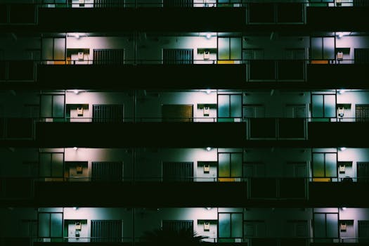 A nighttime view of a modern Tokyo apartment building with glowing lights and geometric patterns.