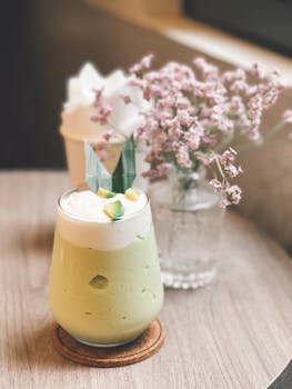 A creamy avocado smoothie served on a wooden table with delicate pink flowers adds charm to any café setting.
