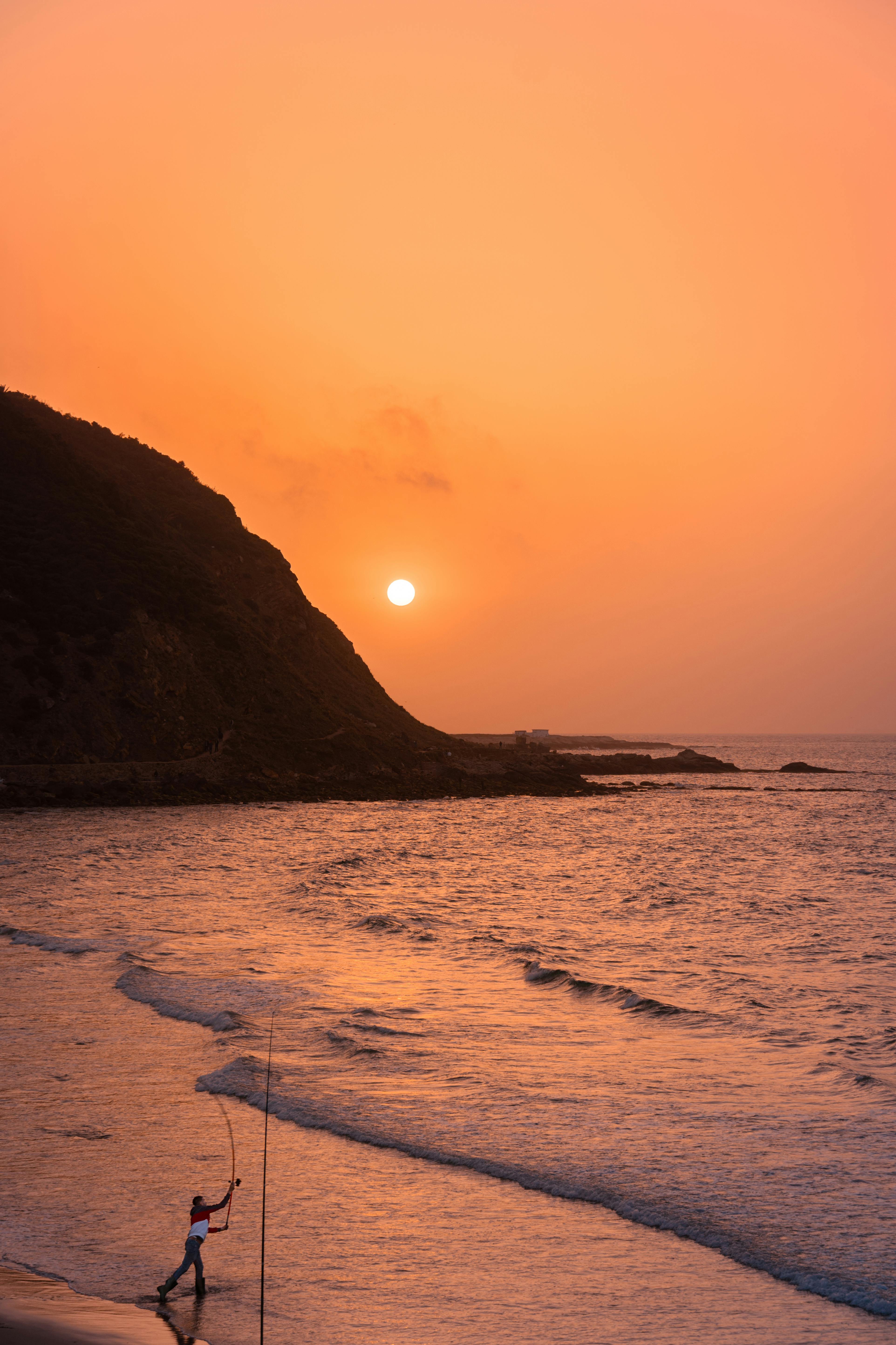 Silhouette of a fisherman casting at sunset on Tangier beach in Morocco.