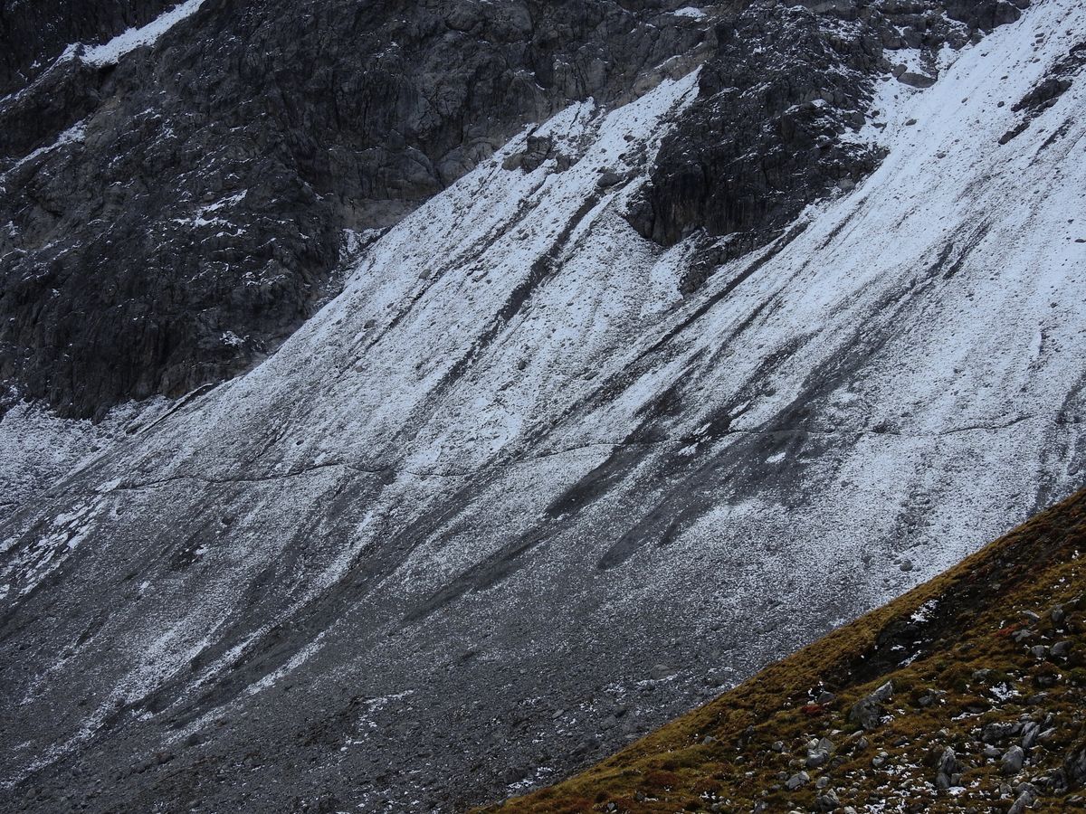 Steep scree and snow-streaked slope beside a mountain trail.