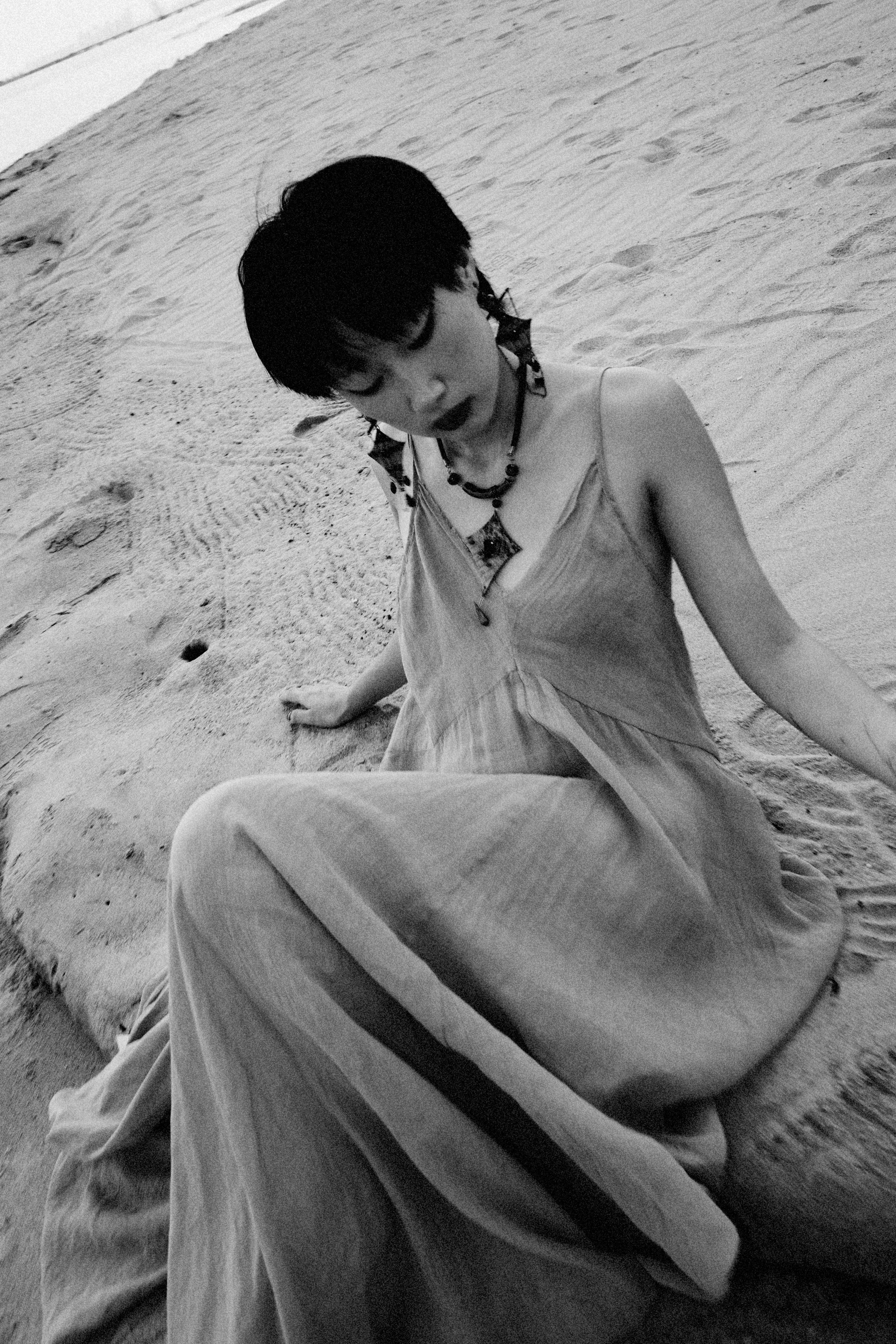 Black and white photo of a woman on a sandy beach, exuding elegance and calm.