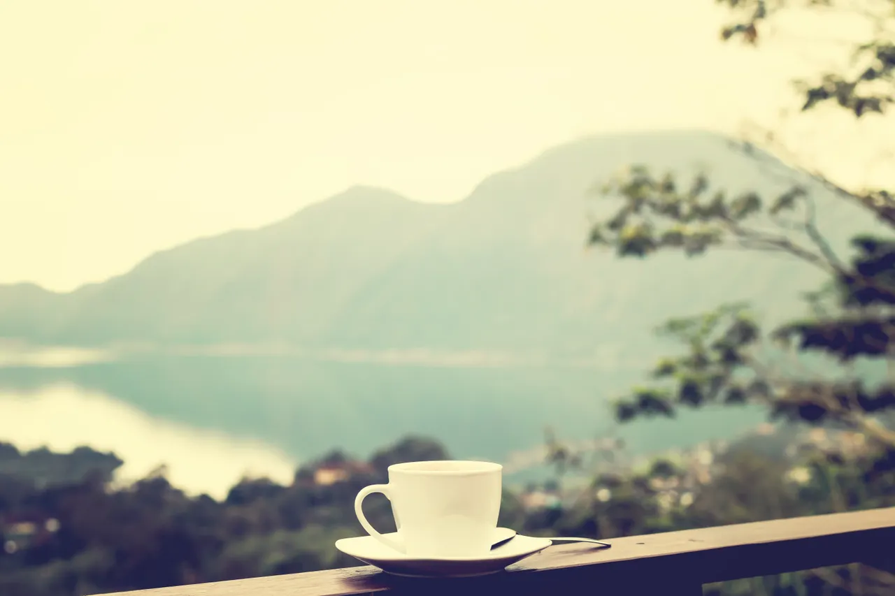 morning-coffee-corner-balcony Coffee cup resting on a balcony railing overlooking the water at sunrise