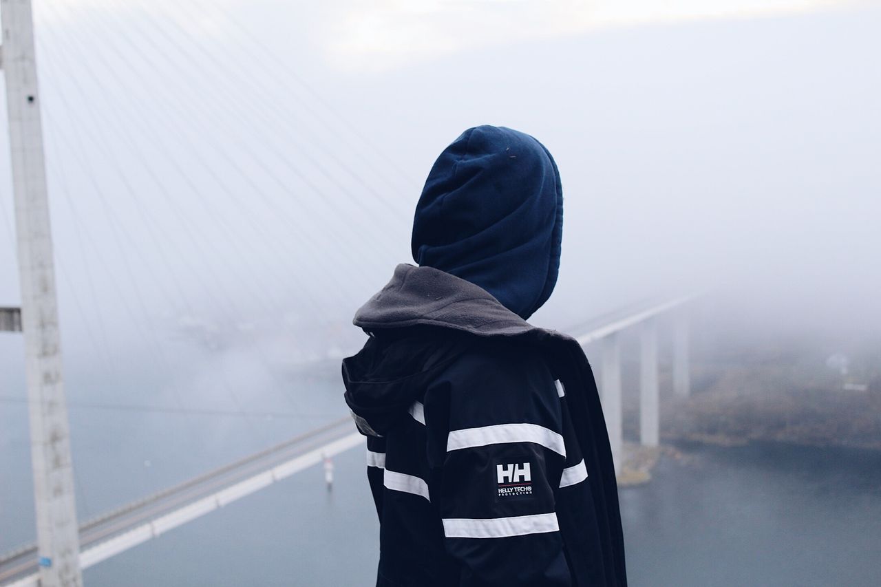a man stands on a foggy suspension bridge wearing a jacket creating a