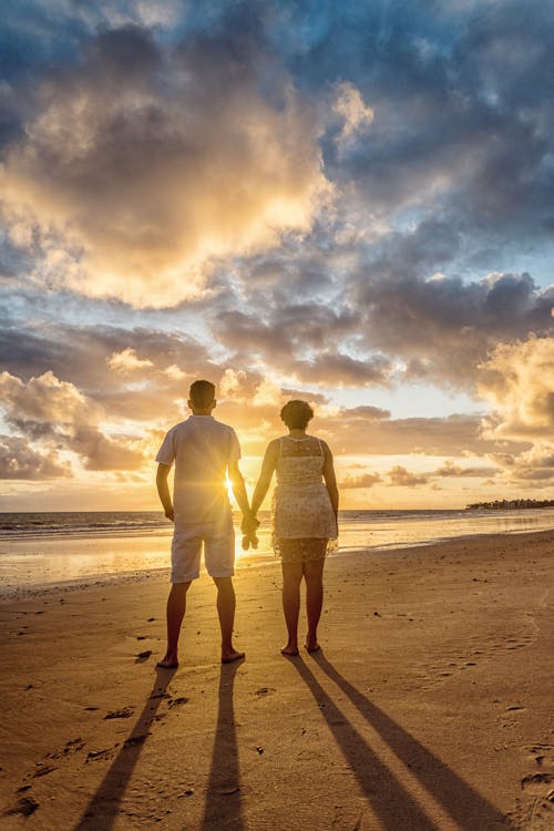 Free Back View Photo of Couple Standing on the Beach Looking at the Horizon Stock Photo