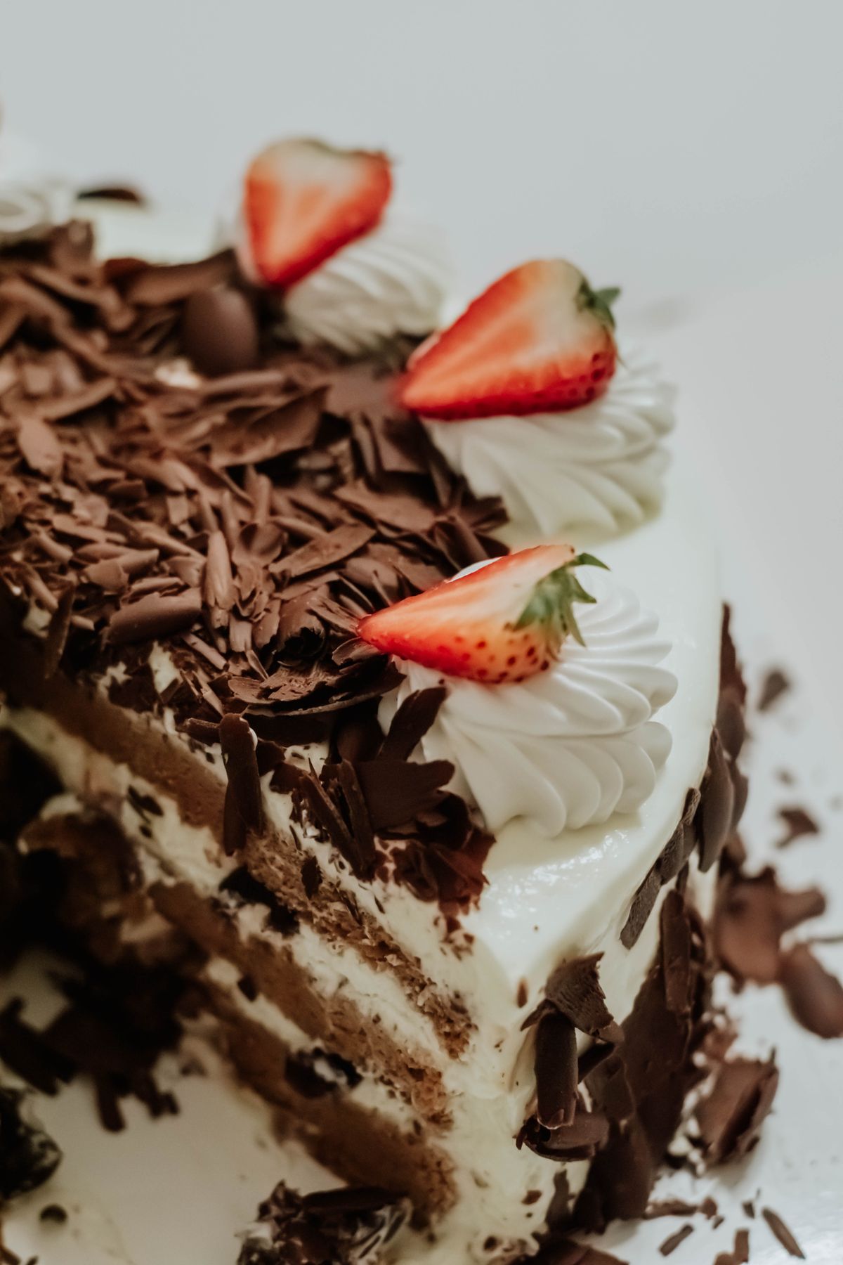Cut layered cream cake with chocolate curls, whipped cream rosettes and strawberry halves