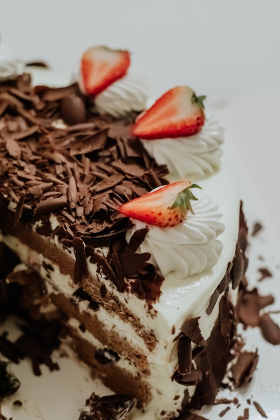 Cut layered cream cake with chocolate curls, whipped cream rosettes and strawberry halves