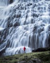 一位身穿红色夹克的徒步旅行者，站在宏伟的瀑布前，捕捉着大自然力量的精髓