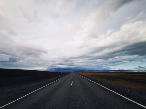 An empty road stretching through the vast Icelandic plains under a cloudy sky.