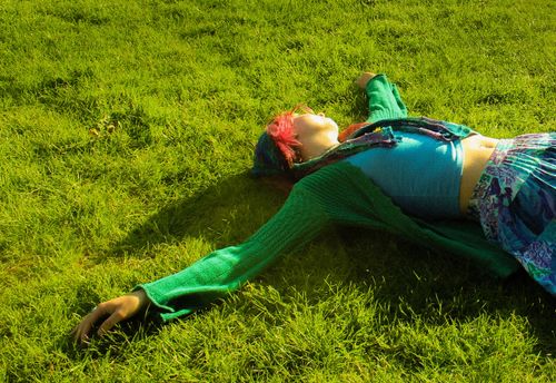Free Woman laying on grass in a vibrant outfit, embracing tranquility and leisure. Stock Photo
