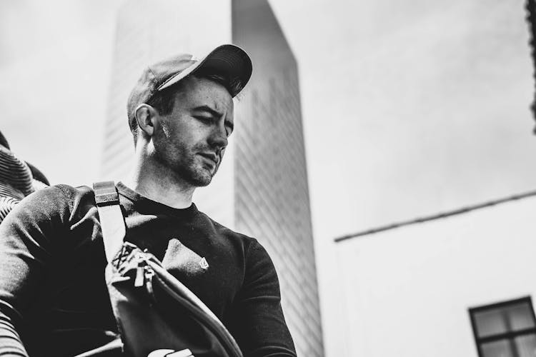 Selective Focus Grayscale Photo Of Man Looking Down With Skyscraper In The Background