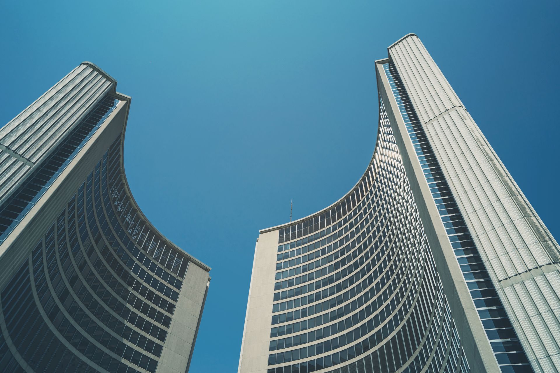 Striking architectural shot of Toronto City Hall's iconic curved buildings against a clear blue sky.