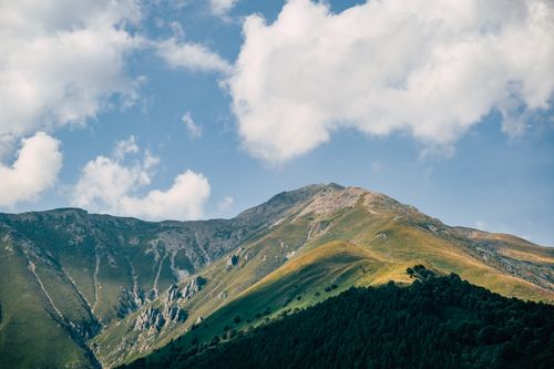 Free Scenic view of towering mountains under a bright blue sky with fluffy white clouds. Stock Photo