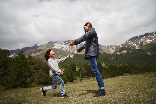 бесплатная Женщина и ребенок играют на зеленой траве у горы Стоковое фото