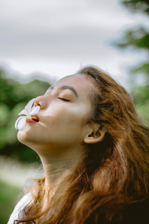 Free Selective Focus Photo of Woman With a White Flower in Her Mouth Posing with Her Eyes Closed Stock Photo