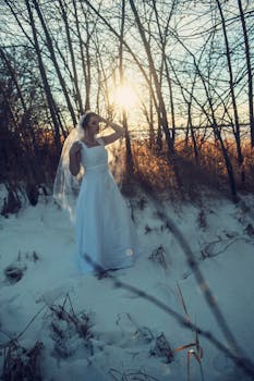 日落时分，身着婚纱的新娘站在白雪皑皑的森林里，宛如宁静的冬日仙境
