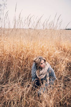 一个女人戴着围巾，蹲在一片高大的金色草地上