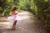 明媚的夏日，一名身穿粉色连衣裙的年轻女子在森林小路上快乐地旋转