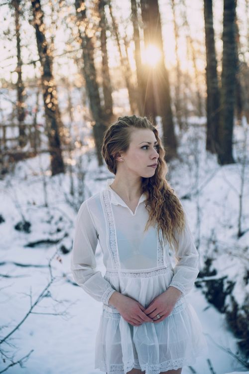 Free A woman in a white dress stands pensively in a snowy winter forest setting. Stock Photo