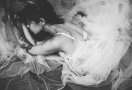 一幅黑白肖像中，一位身着优雅新娘装的女人正优雅地躺着