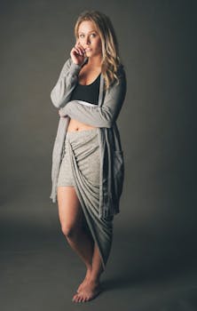 一位时尚女士赤脚站在柔和的灰色背景前，身着舒适的休闲装