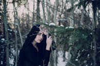 一位神秘女子留着深色长发，站在白雪皑皑的冬季森林中，四周树木环绕