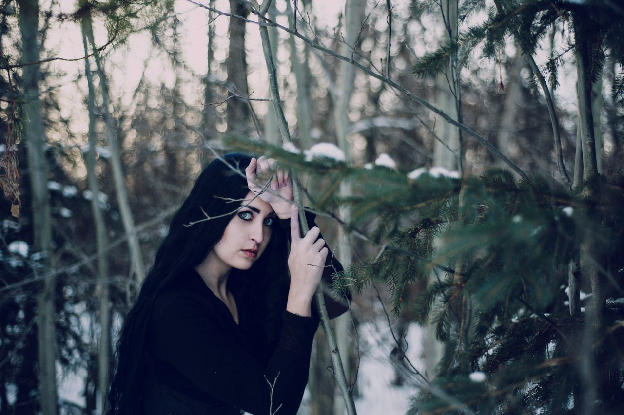 a mysterious woman with long dark hair stands in a snowy winter forest