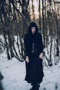 白雪皑皑的森林中，一位身着黑衣的哥特妇女静静站立，营造出神秘的冬日景象