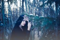 一名黑发女子透过白雪皑皑的森林枝桠凝望，营造出神秘的氛围