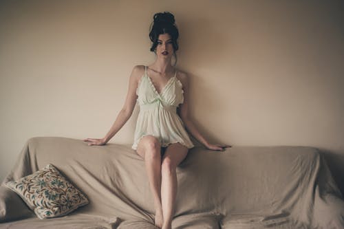 Photo of Beautiful Woman in White Night Dress Sitting on Top of Sofa Backrest