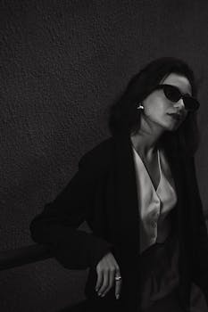 Black and white portrait of an elegant woman wearing sunglasses and a sophisticated outfit.