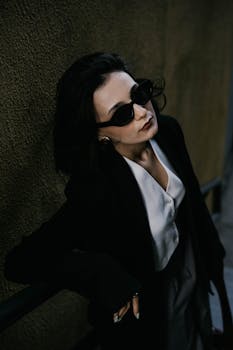 Elegant woman in sunglasses and formal attire poses against urban backdrop in Baku.