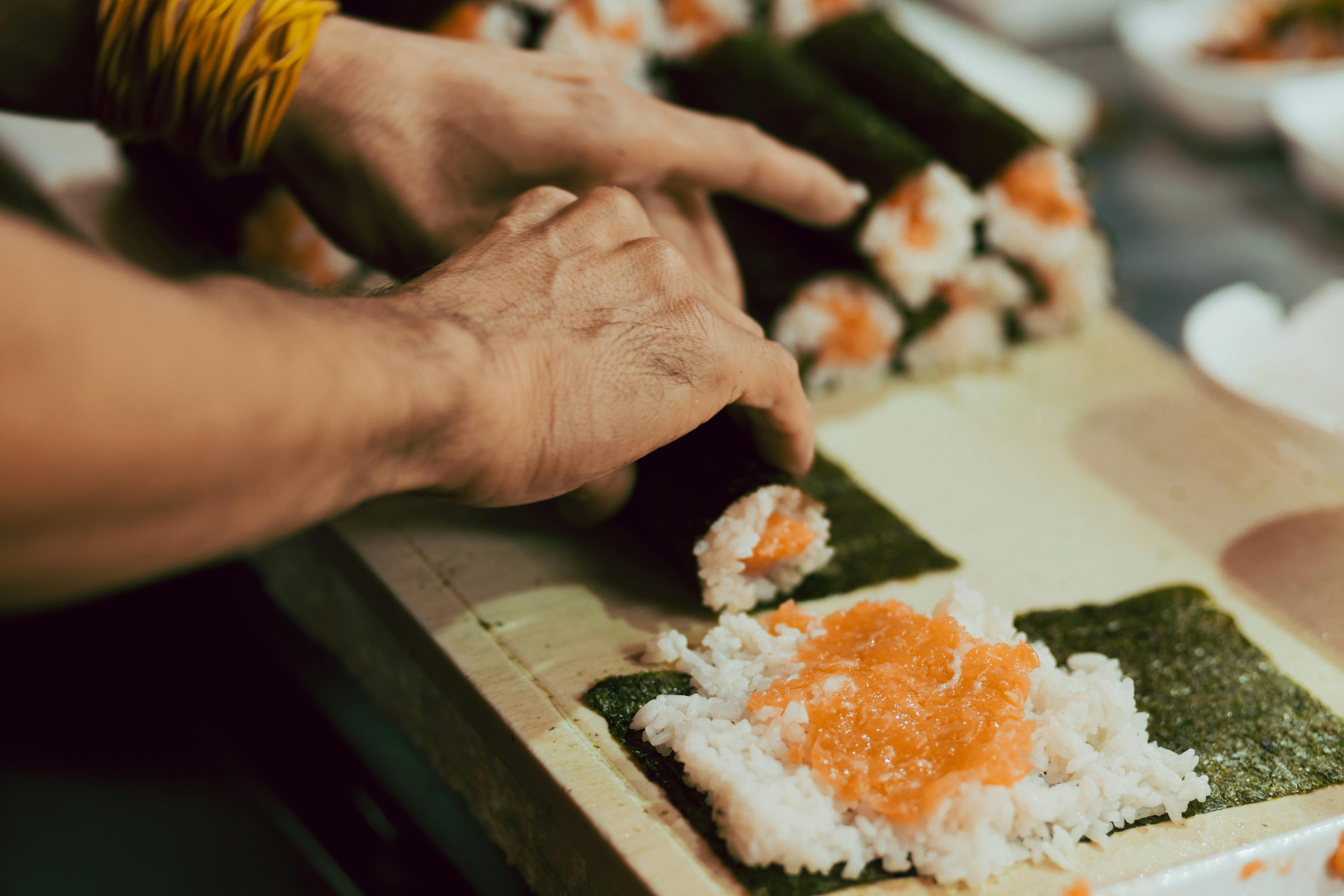 Close-up of sushi preparation with rice and salmon on seaweed, showcasing Japanese cuisine.
